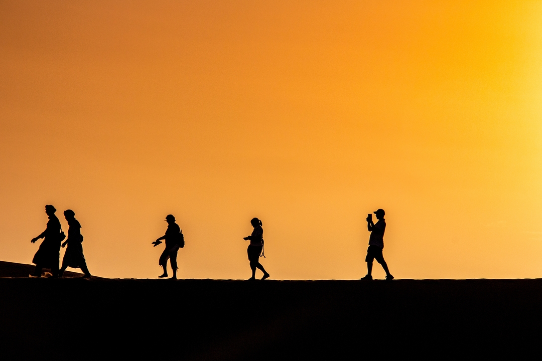 Silhouettes de personnes marchant sur une dune pendant le coucher du soleil.