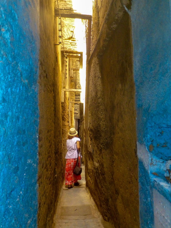 Personne marchant dans une ruelle étroite aux murs bleus.