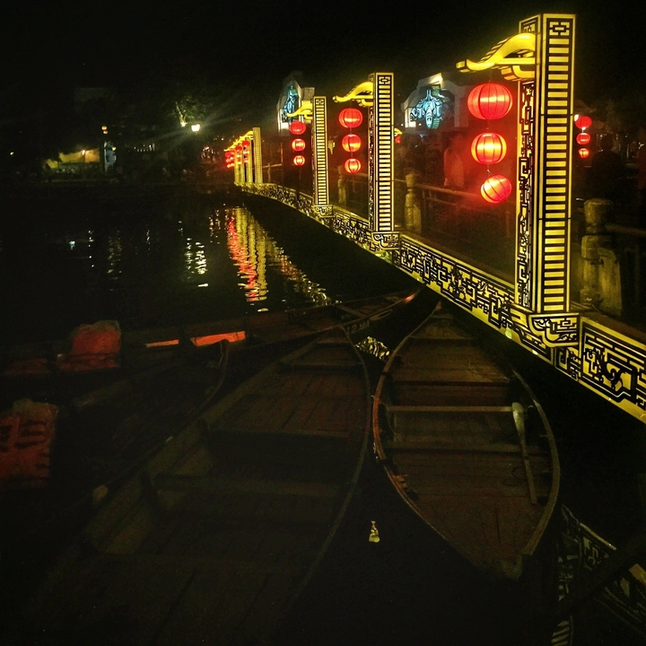Bateaux en bois sur une rivière la nuit, illuminés par des lumières décoratives.