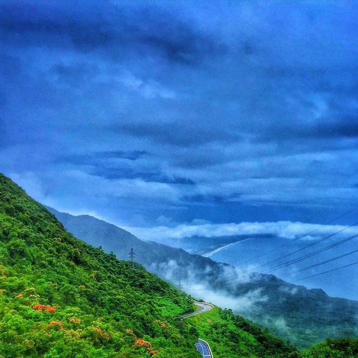 Ciel nuageux au-dessus de collines verdoyantes et de montagnes.