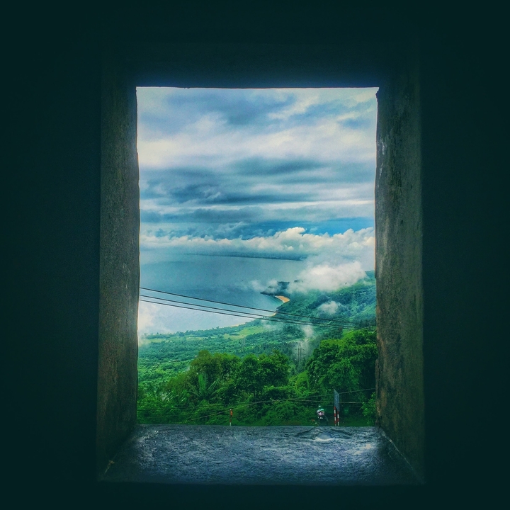 Vue panoramique d'une côte depuis une position élevée, avec des nuages et l'océan.