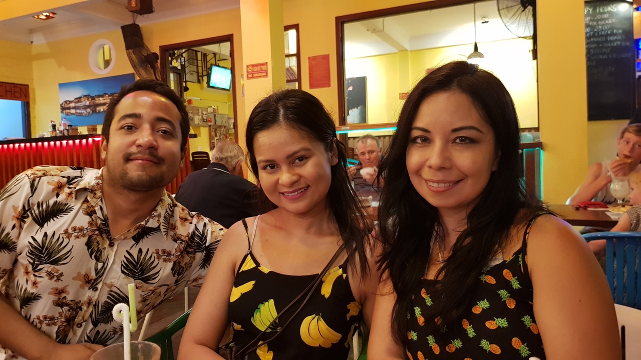 Trois personnes souriantes dans un restaurant à l'atmosphère animée.