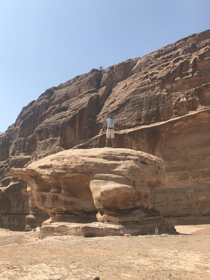 Individu debout sur un rocher avec les bras ouverts dans un terrain désertique.