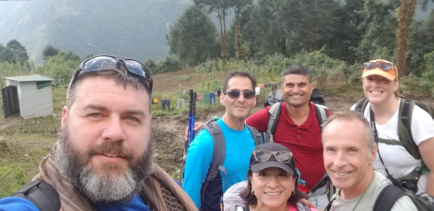 Groupe de randonneurs posant en plein air avec des arbres et des montagnes en arrière-plan.
