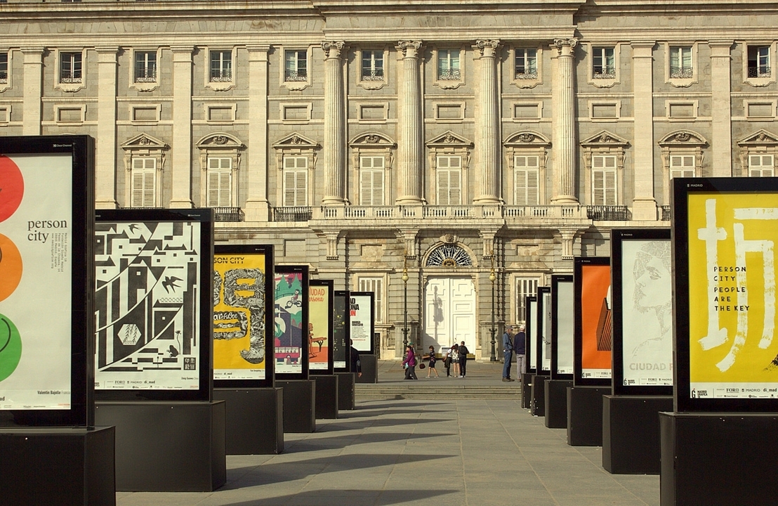 Une exposition en plein air avec des affiches colorées et un grand bâtiment en arrière-plan.