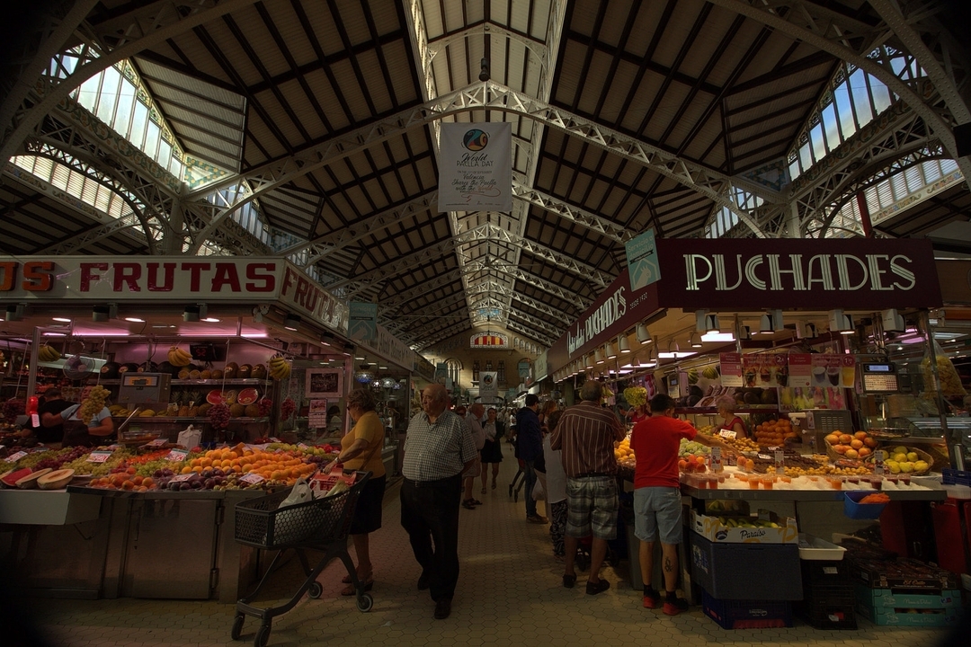 Intérieur d'un marché animé avec des étals de fruits et légumes.