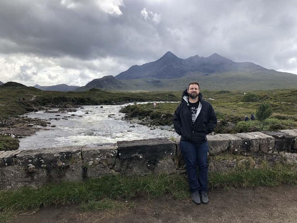 A person standing on a bridge with mountains in the background.
