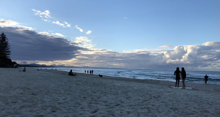 Plage de sable avec des gens et un ciel dramatique.