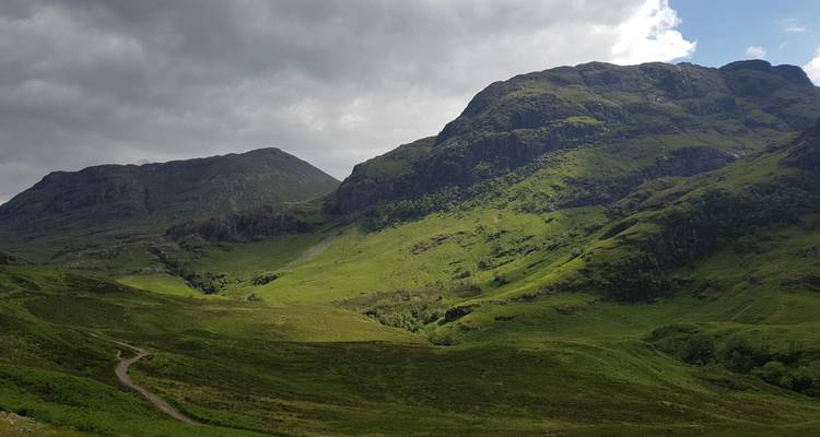 Vista panorámica de colinas verdes y montañas rocosas bajo un cielo nublado.