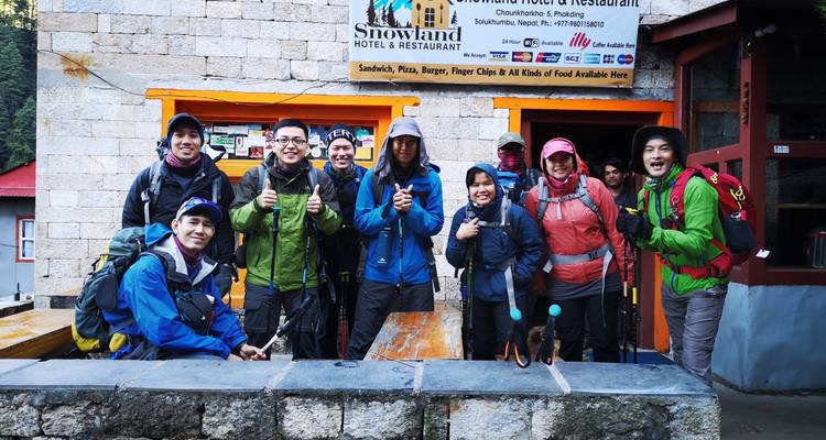 Group of hikers with trekking poles posing outside a restaurant.