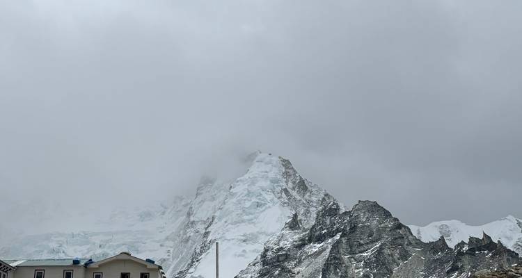 Camp at the base of a snowy mountain with clouds overhead.
