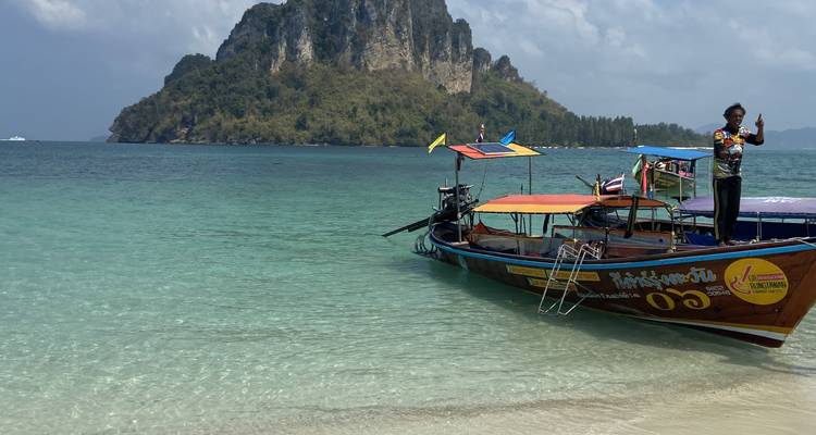 Longtail boats anchored along a tropical beach with clear water.