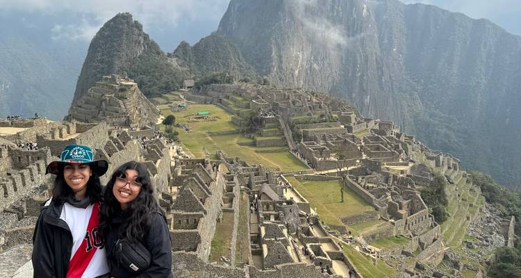 Two people smiling at Machu Picchu with a view of the ruins.