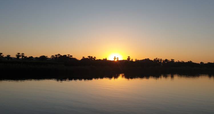 Coucher de soleil sur une rivière avec des arbres en silhouette.