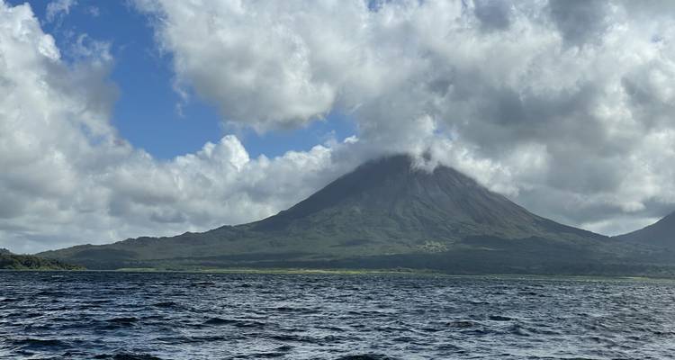 Volcán Arenal elevándose sobre un lago bajo un cielo nublado.