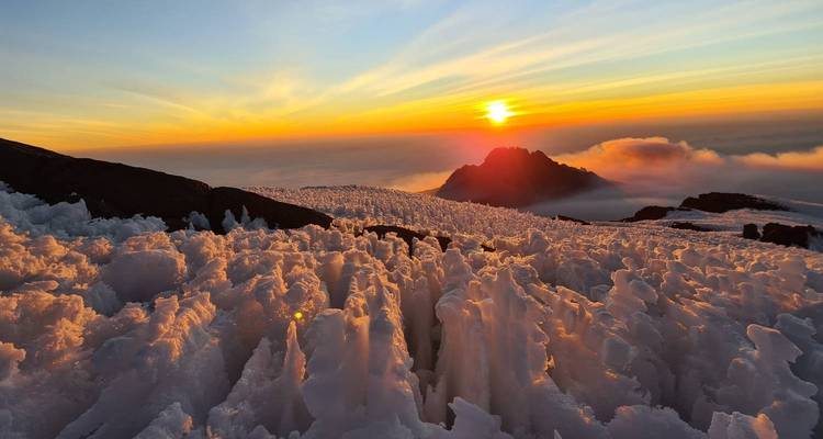 Montagne enneigée avec un lever de soleil et des nuages en arrière-plan.