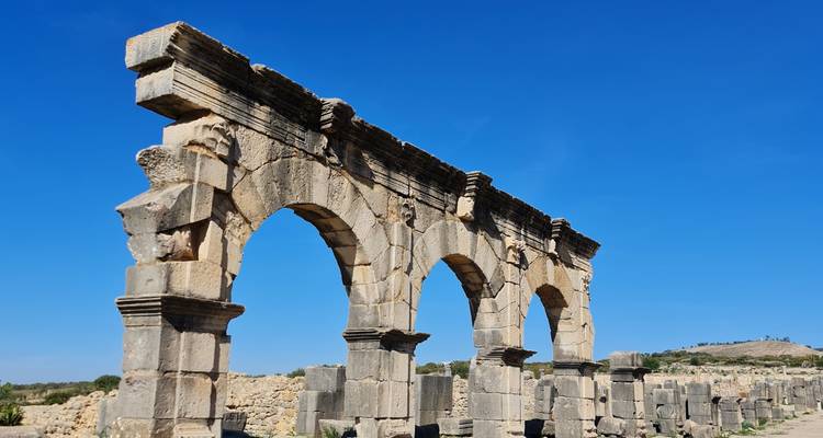 Arches romaines dans une ruine antique sous un ciel bleu.