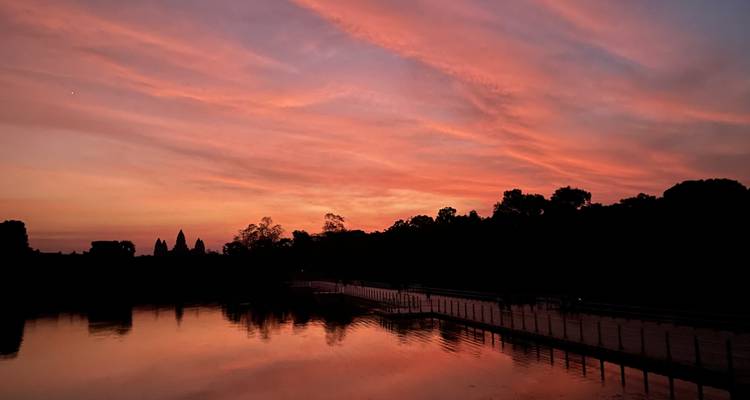 Silueta de ruinas de templo contra una puesta de sol colorida.