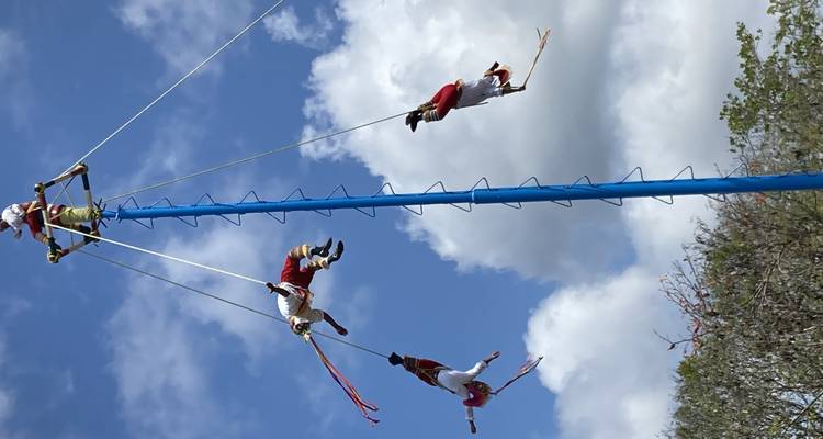 Performers in traditional costumes suspended on a pole in an aerial dance.