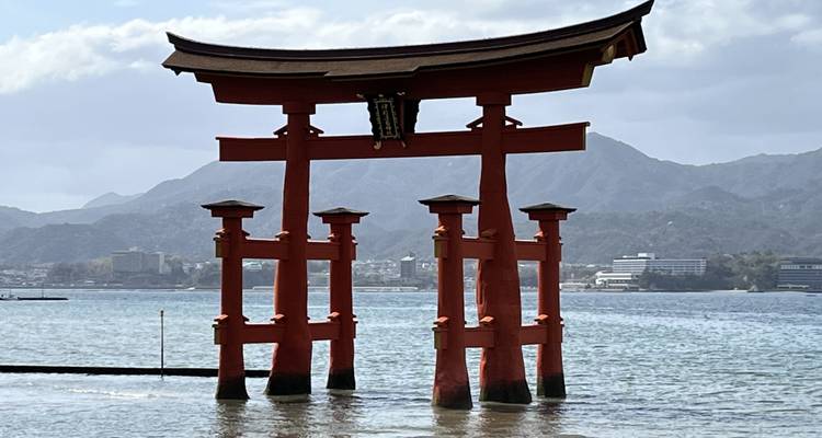 Emblématique torii vermillon du sanctuaire d'Itsukushima se dressant dans la mer avec un arrière-plan montagneux.