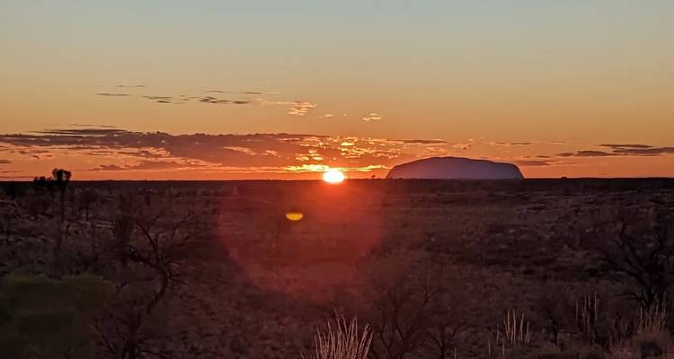 Lever de soleil sur un paysage plat avec une formation rocheuse au loin.