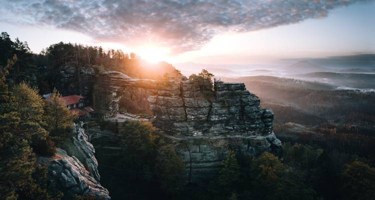 Dramatic sunrise over a rocky landscape with a house nestled on the cliffs.