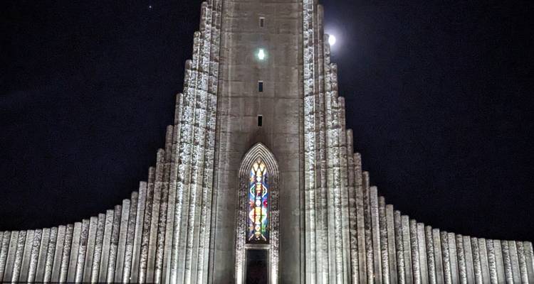 Vue nocturne de la Hallgrímskirkja illuminée avec la lune visible.