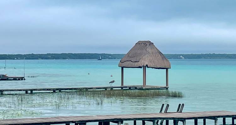 Wooden jetty leading into a turquoise lake with a thatched hut.