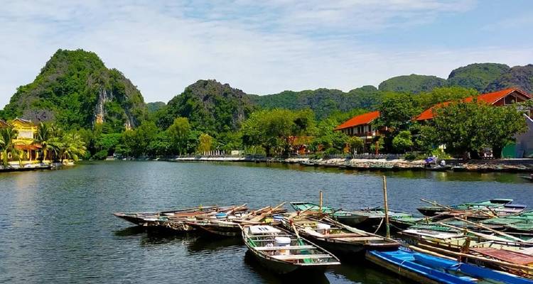 Rowboats anchored on a serene river with houses and temples.