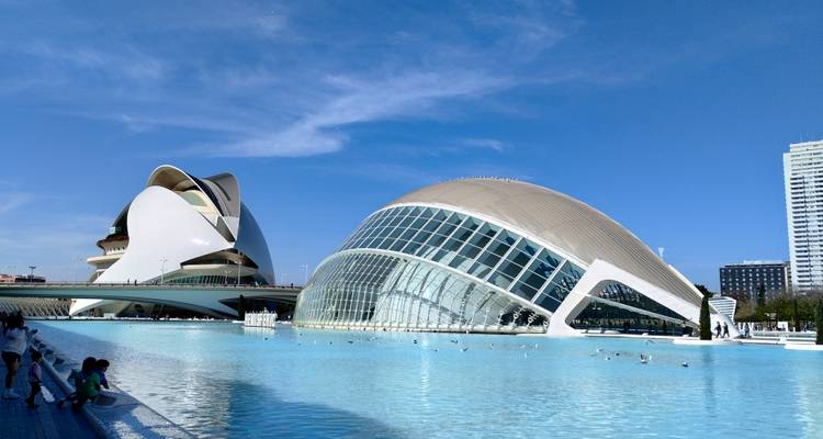 Modern buildings with reflections in water under a clear blue sky.