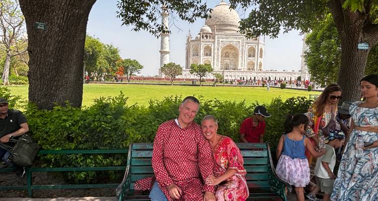 A couple sitting on a bench with the Taj Mahal in the background.