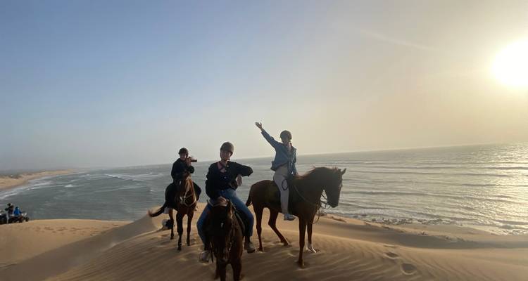 Mensen te paard rijdend op duinen met zee op de achtergrond.