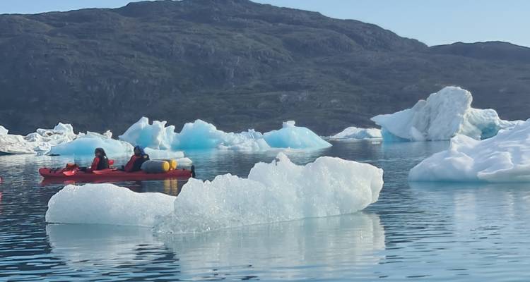 Kayakers paddling near iceberg in a serene setting.