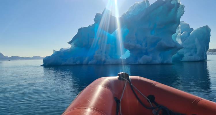 Iceberg in calm waters with sunlight streaming through.