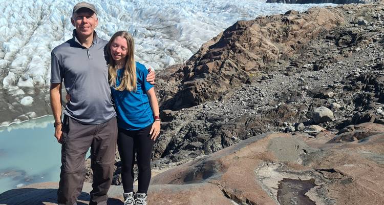 Two people smiling with a glacier and rocky terrain in the background.
