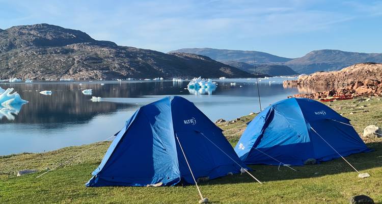 Two tents set up on grass with icebergs and mountains in the background.
