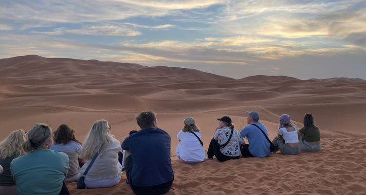 A group watching the sunset over sand dunes in the desert.