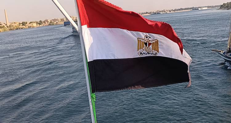 Egyptian flag waving on a ship with a river scene.