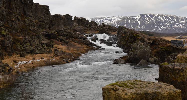 Fluss, der durch felsige Landschaft mit schneebedeckten Bergen fließt.