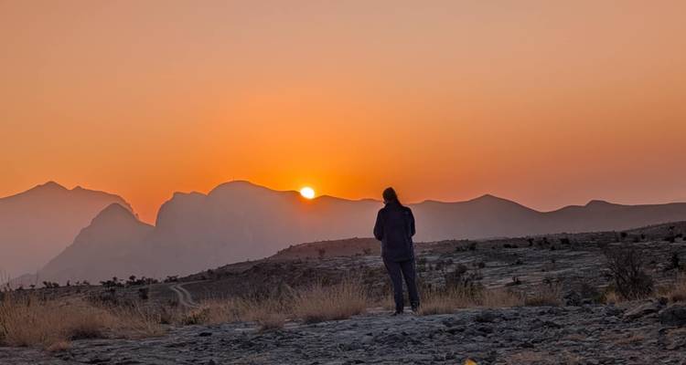 Een persoon die naar een zonsondergang kijkt boven bergen in een woestijn.