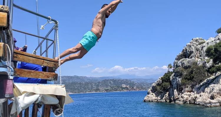 Mann, der von einem Boot ins Meer springt, mit Klippen im Hintergrund.
