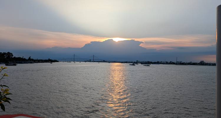 Sunset over a river with boats and a bridge in the distance.