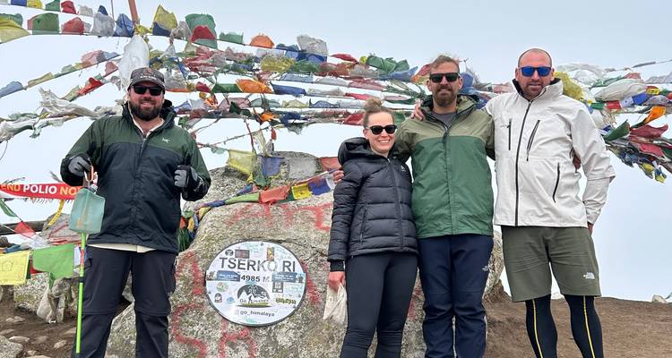Hikers posing with prayer flags on a mountain summit.