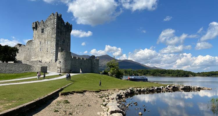 Château historique au bord d'un lac avec des gens qui se promènent à proximité.