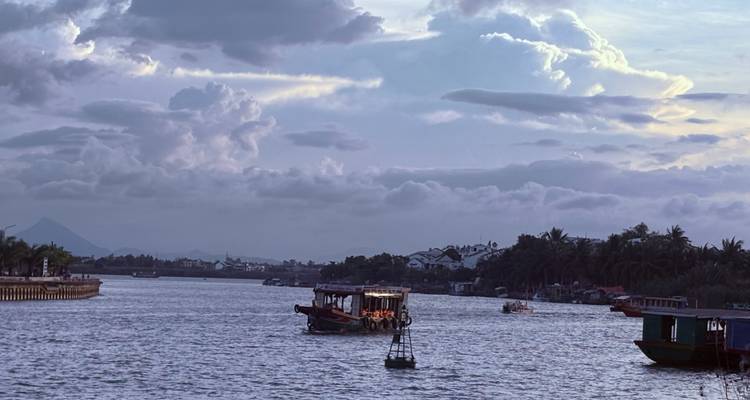 Boats on a river at dusk with a cloudy sky.