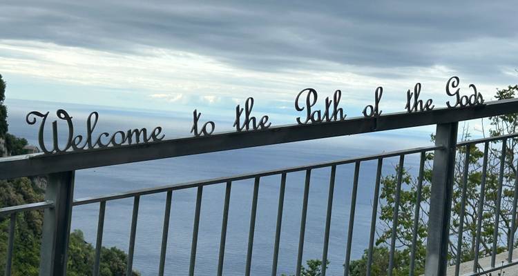 A sign reading 'Welcome to the Path of the Gods' with a sea view.