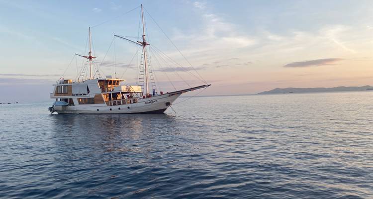 Sailing boat on calm waters at sunset with an island in the distance.