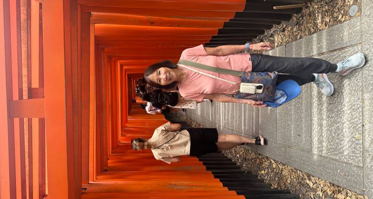 Tourist smiling in a corridor lined with red wooden torii gates.
