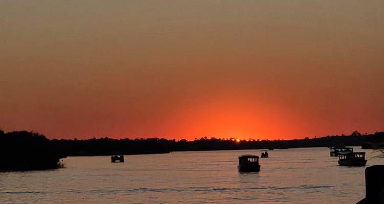 Coucher de soleil sur une rivière avec de petits bateaux en silhouette.