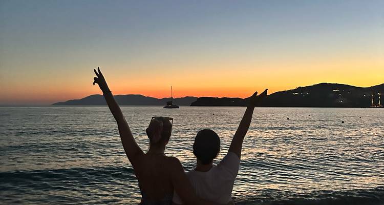 Deux personnes sur une plage au coucher du soleil faisant des signes de paix.